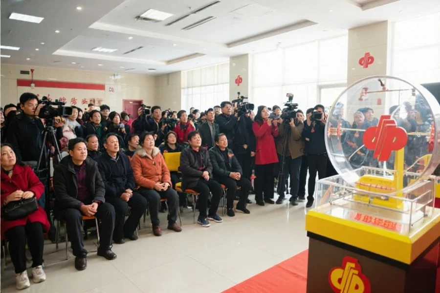 一群市民与媒体记者在明亮的大厅内观看彩票摇号现场直播，大家表情认真，现场气氛庄重